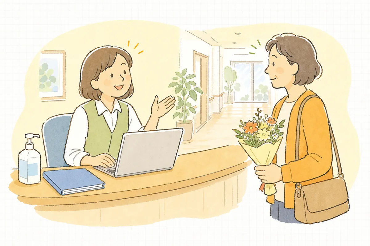 介護施設の受付カウンターで、面会に来たご家族を笑顔で迎え、予約表を確認している事務担当者